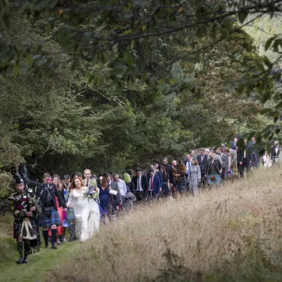 Wedding guests following the piper through the estate.